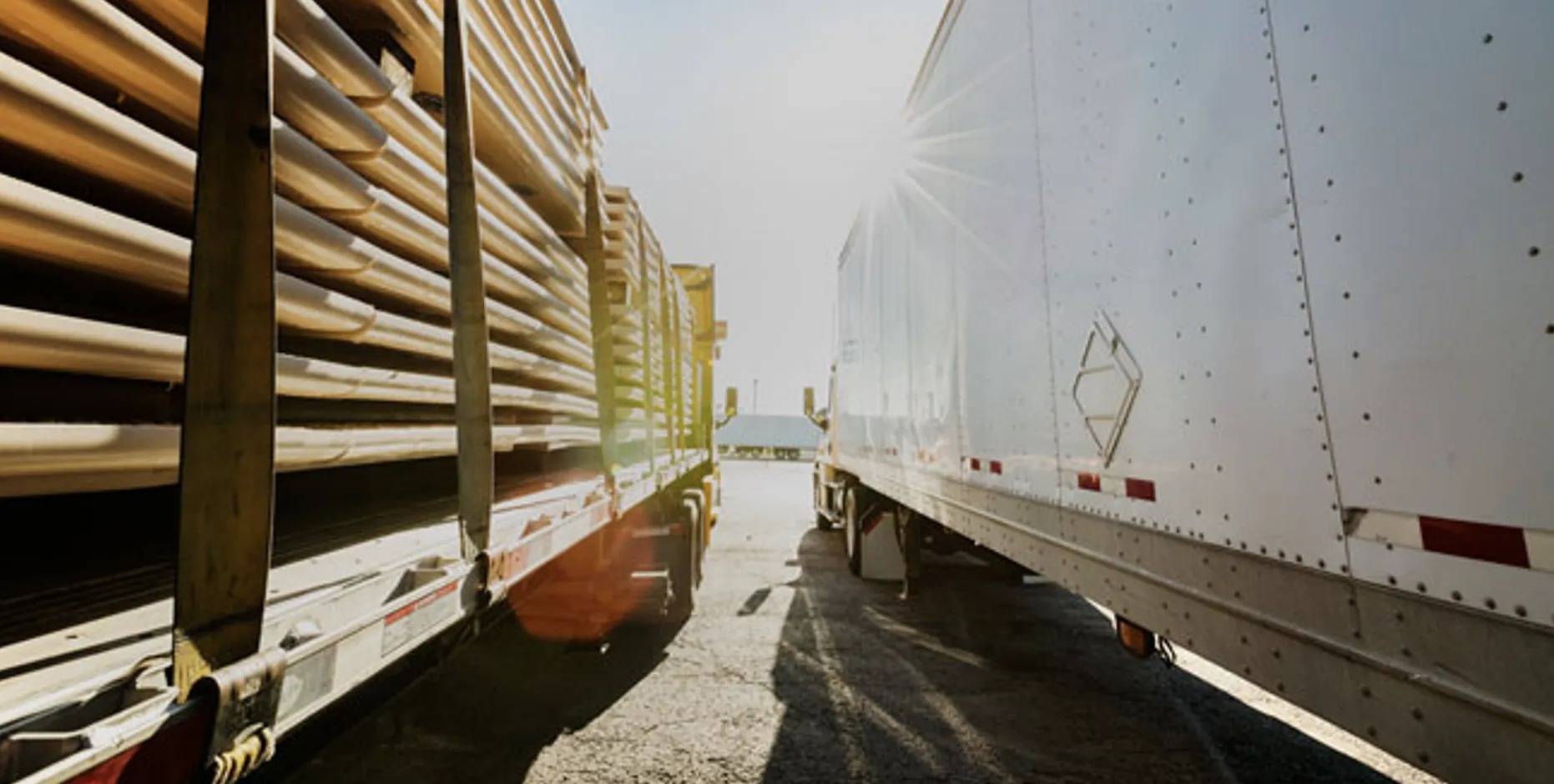 A flatbed trailer loaded with industrial materials beside a white semi-trailer